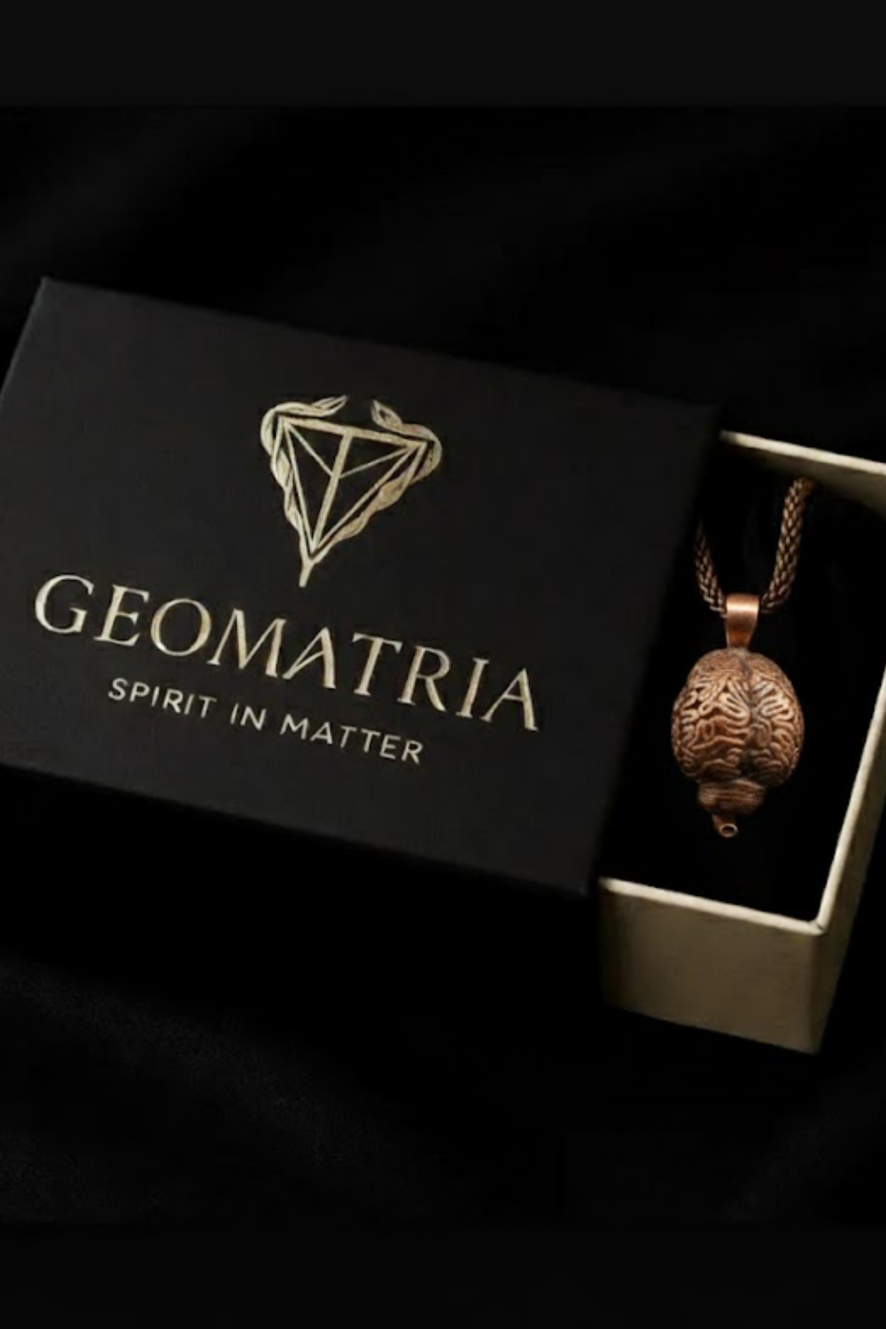 A black box with the word "GEOMATRIIA" printed on it, along with a pendant necklace inside the box.