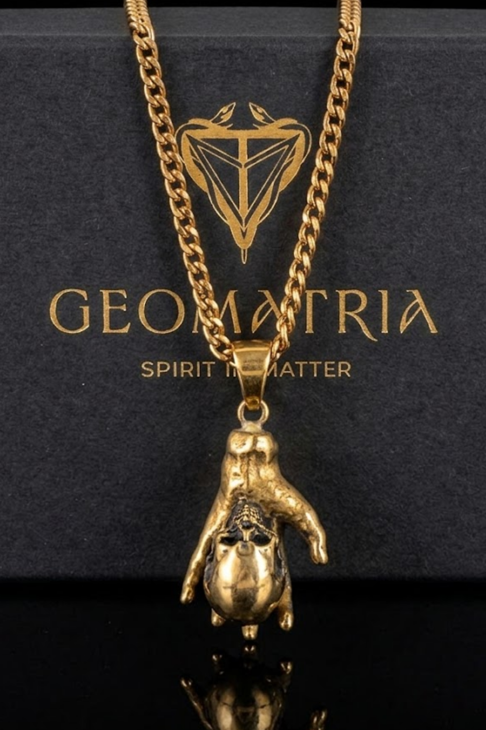 A gold-colored pendant necklace with a unique design, displayed on a black background with the text "Geomatria" and "Spirit in Matter" printed on it.