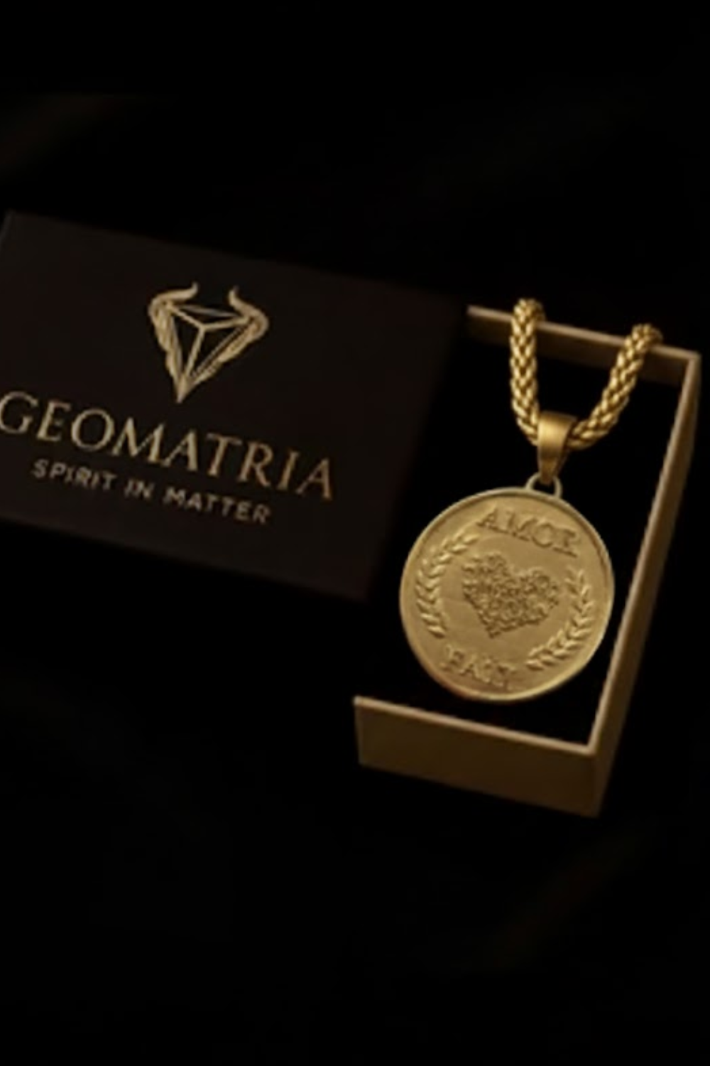 A gold-colored necklace with a pendant is displayed in a black box with the text "Geomatria" and "SPIRIT IN MATTERS" printed on it.