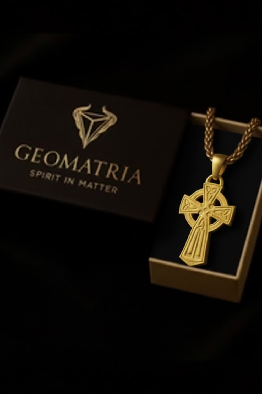 A gold cross pendant is displayed in a gold box with the text "Geomatria Spirit in Matter" printed on it.
