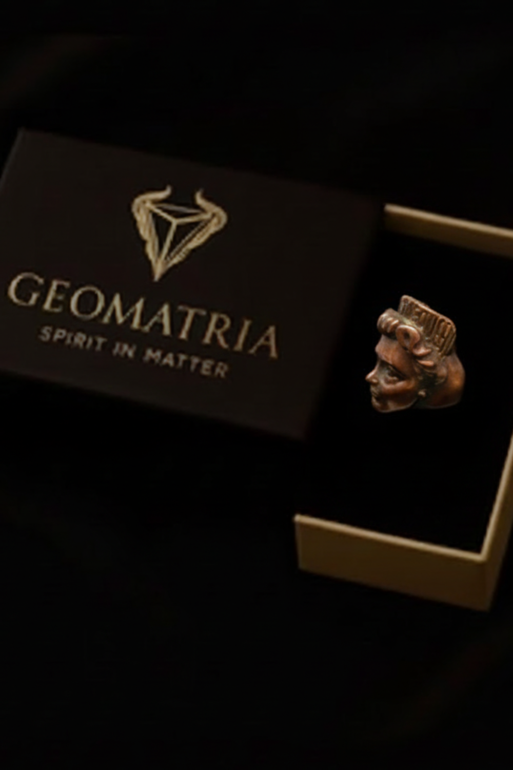 a ring with a geometric design, placed inside a box with a gold-colored lid.