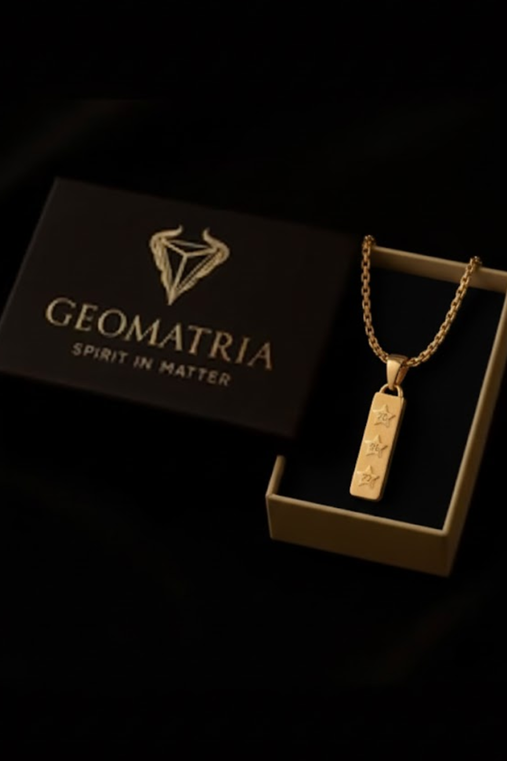 A gold necklace with a pendant is displayed in a black box with the text "Geomatria" and "SPIRIT IN MATTERS" printed on it.
