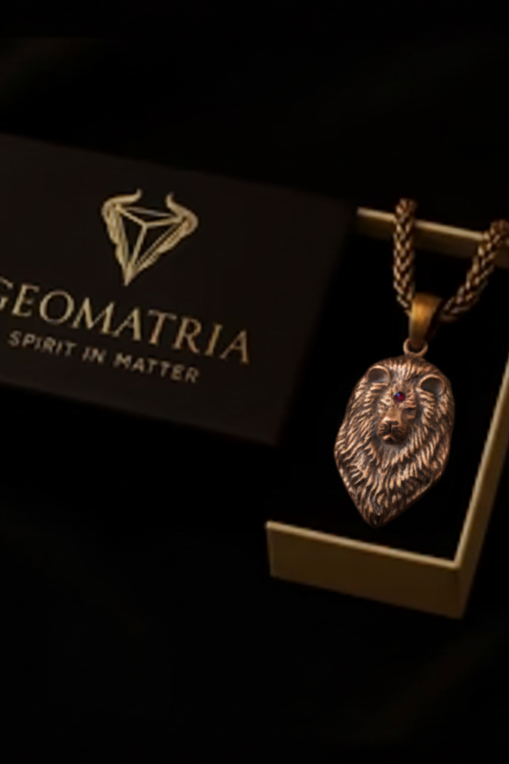 a pendant with a lion's head design, displayed in a box with the text "Geomatria" and "SPIRIT IN MATER".