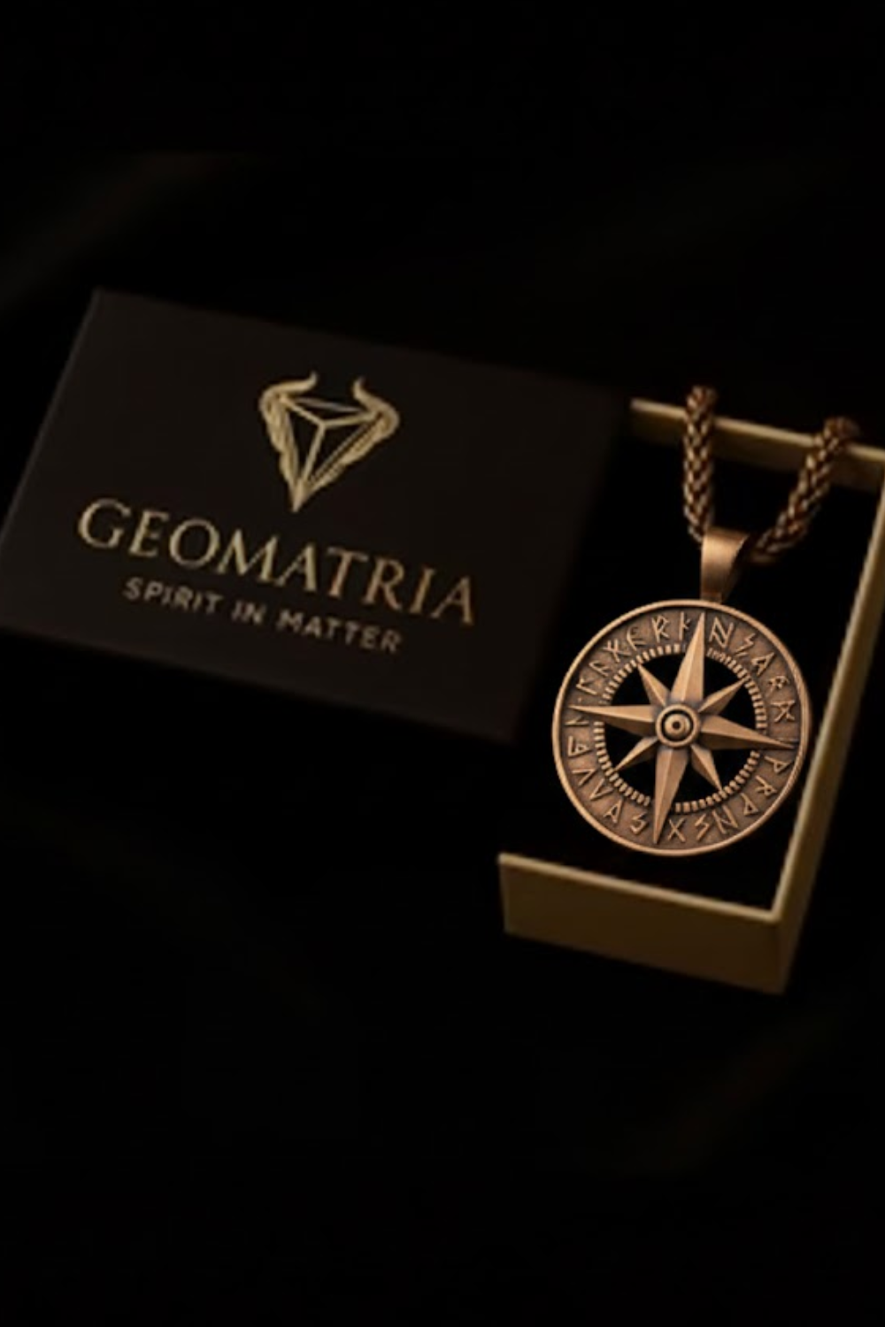 a pendant with a compass design, placed inside a box with the word "Geomatria" written on it.