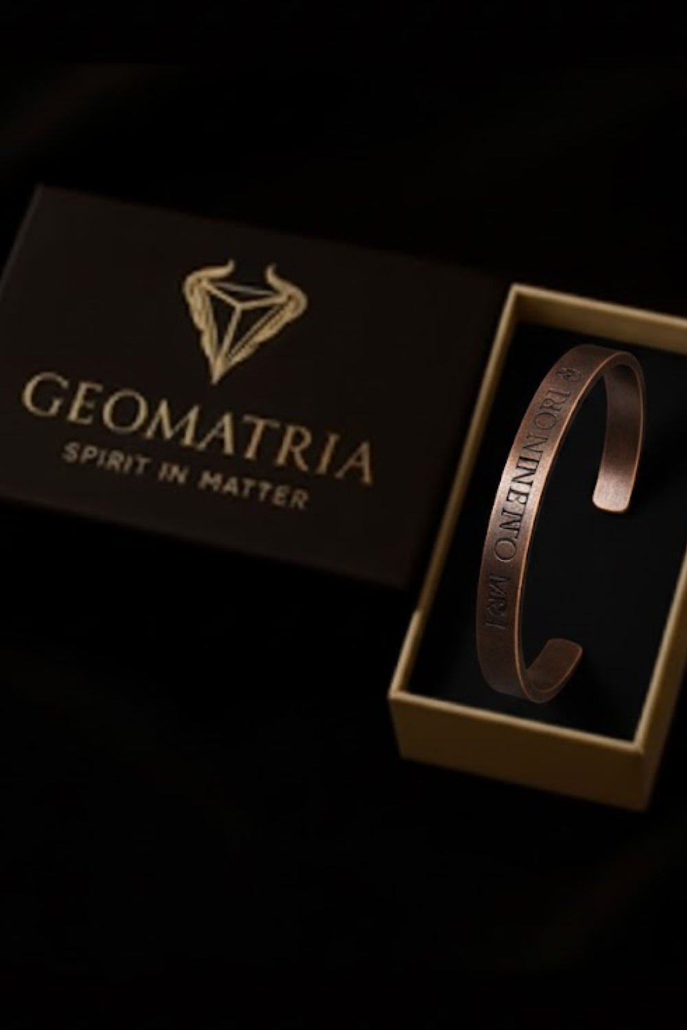 A copper bracelet is displayed in a gold box with the text "Geomatria" and "SPIRIT IN MATTERS" printed on it.