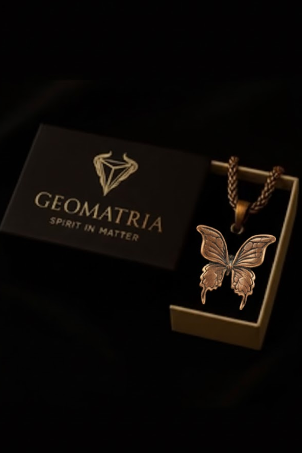 A black box with the word "Geomatria" printed on it, along with a silver butterfly pendant hanging from a chain.