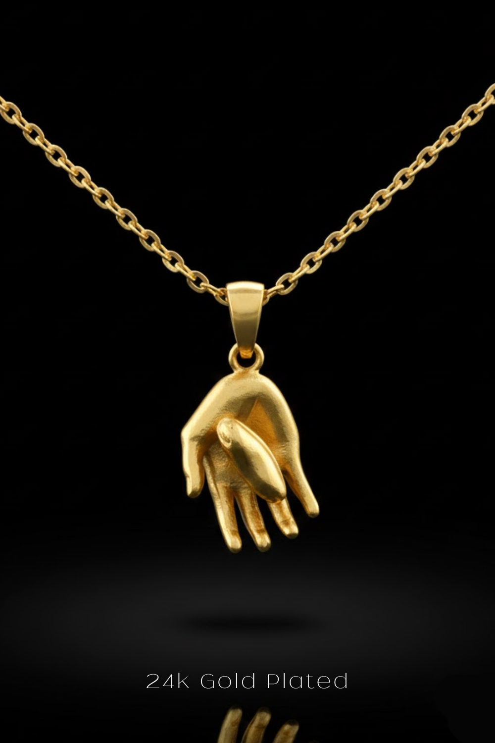 A 24k gold plated pendant in the shape of a hand is displayed against a black background.