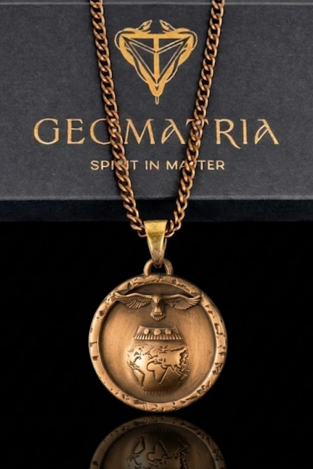 A gold-colored pendant necklace with a circular medallion featuring an image of a globe and a bird, suspended from a chain.
