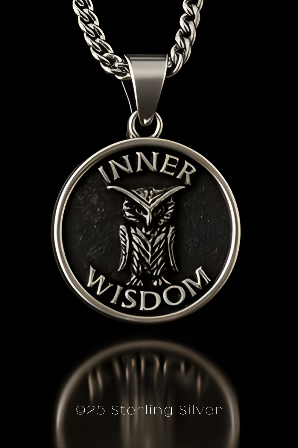 A silver pendant with the text "INNER WISDOM" and an owl design, hanging from a chain against a black background.