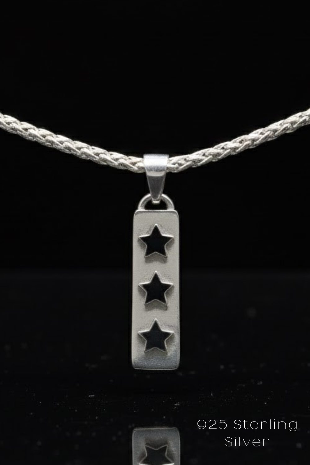 A silver pendant with three stars is suspended from a silver chain against a black background.