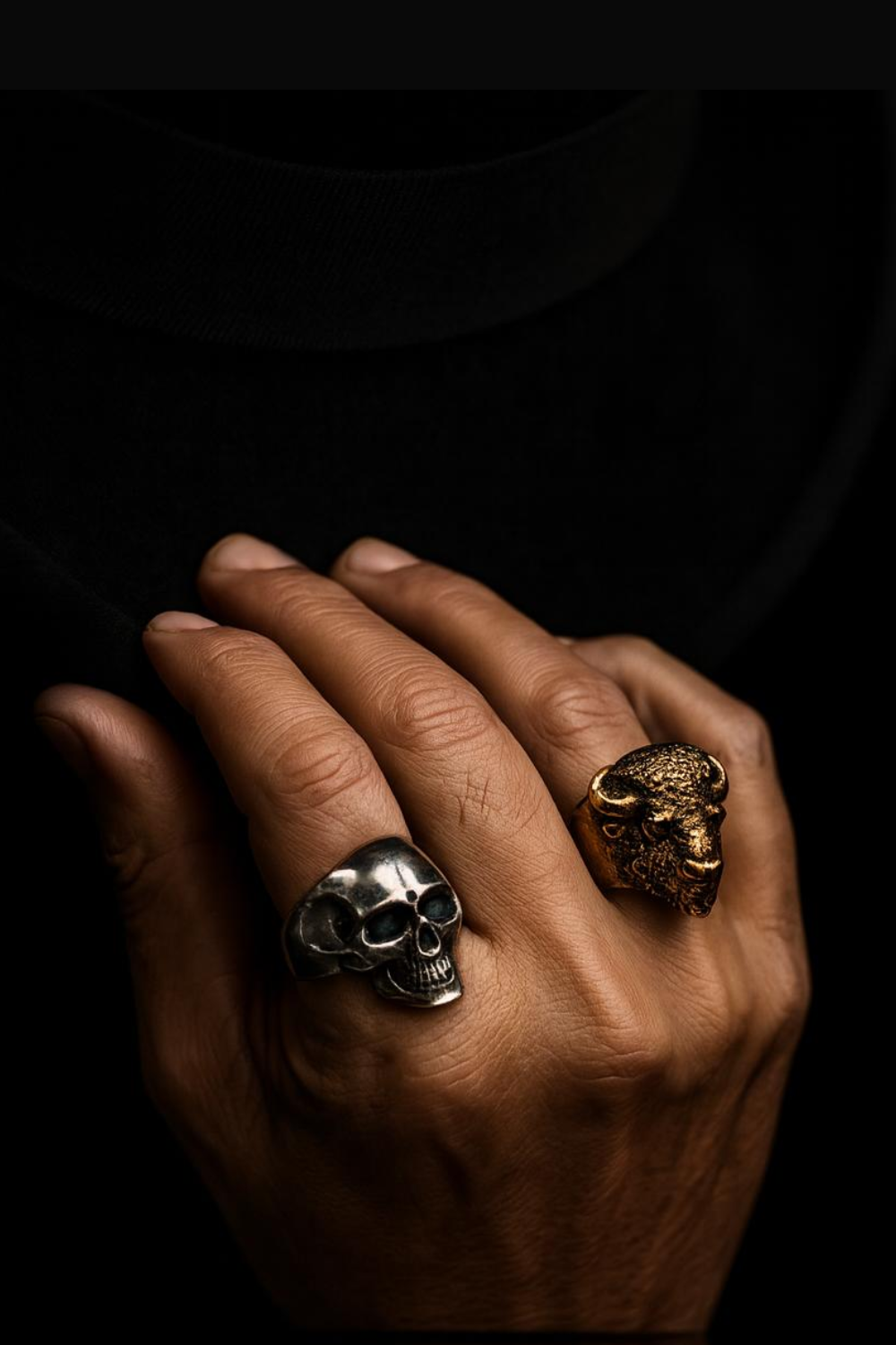 A close-up of a person's hand wearing two rings, one with a skull design and the other with a buffalo head design.