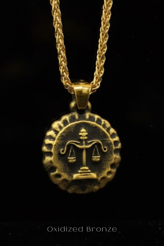 A gold-colored pendant necklace with a circular medallion featuring a symbol of justice, such as scales of justice, suspended from a chain.