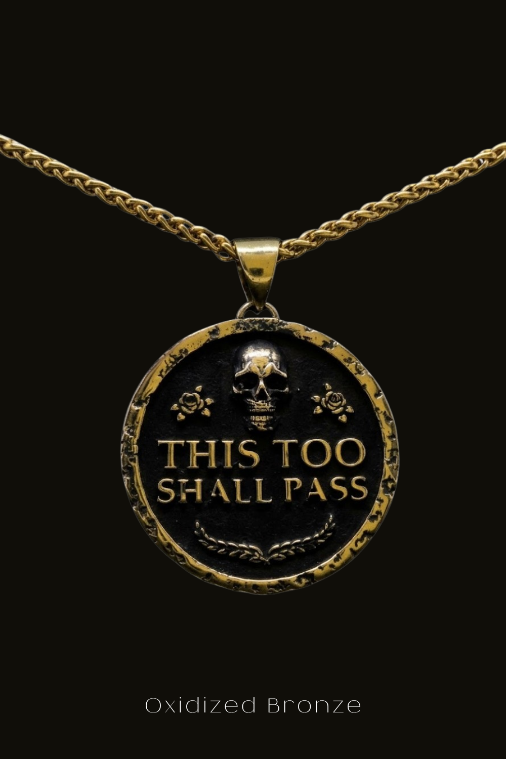 a pendant with the text "THIS TOO SHALL PASS" engraved on it, surrounded by a decorative border.