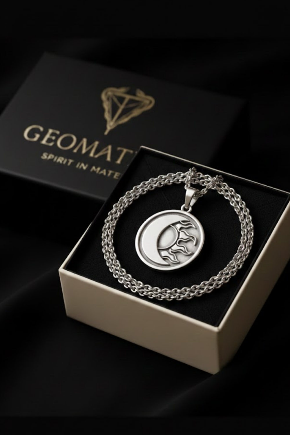 A silver necklace with a pendant featuring a crescent moon and a sun-like symbol, displayed in a black box with a gold-colored logo.