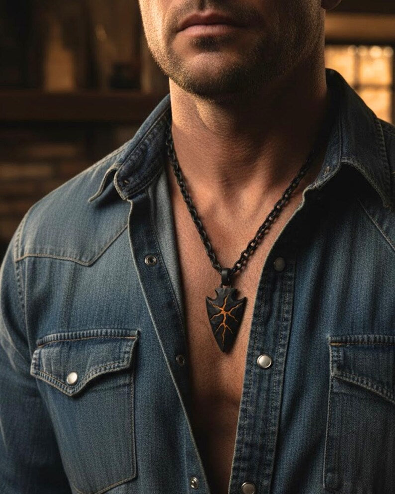 A close-up of a man wearing a denim shirt and a necklace with a pendant.