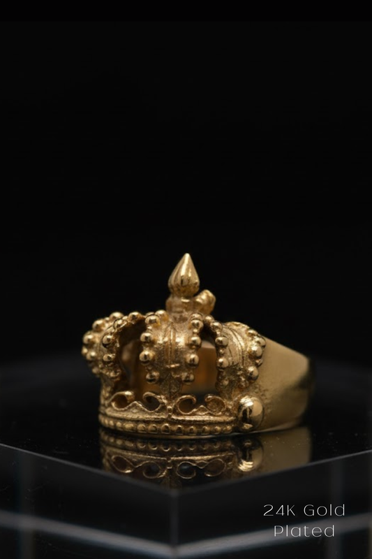 A gold crown ring with intricate details and a pointed top is displayed against a black background.