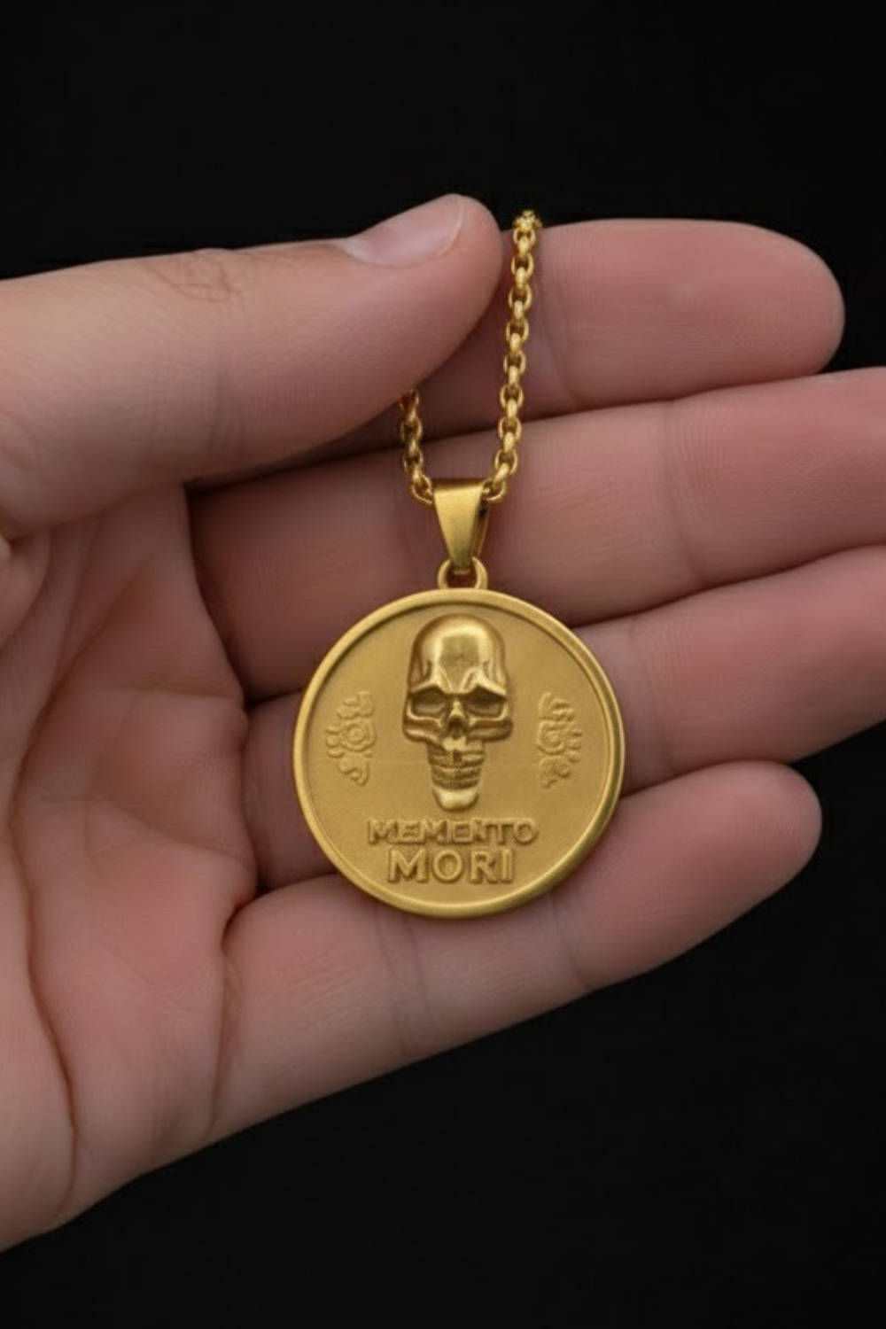 A gold-colored pendant necklace with a round medallion featuring a skull and the Latin phrase "Memento mori" (which means "Remembering the dead" in English).
