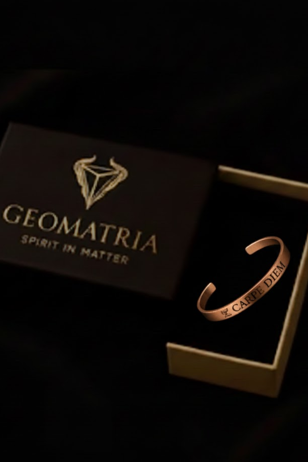 a black box with the word "GEOMATRIIA" written on it, along with the phrase "SPIRIT IN MATERIA" below it. There is also a gold-colored bracelet placed inside the box, which has the text "CARPE DIEM" engraved on it.