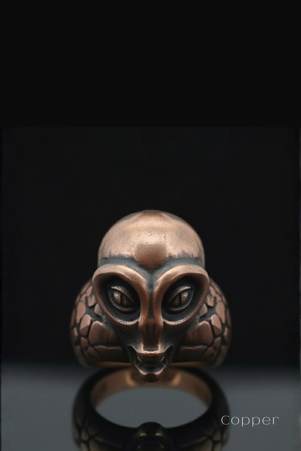 a copper ring with an alien-like face design, set against a black background.