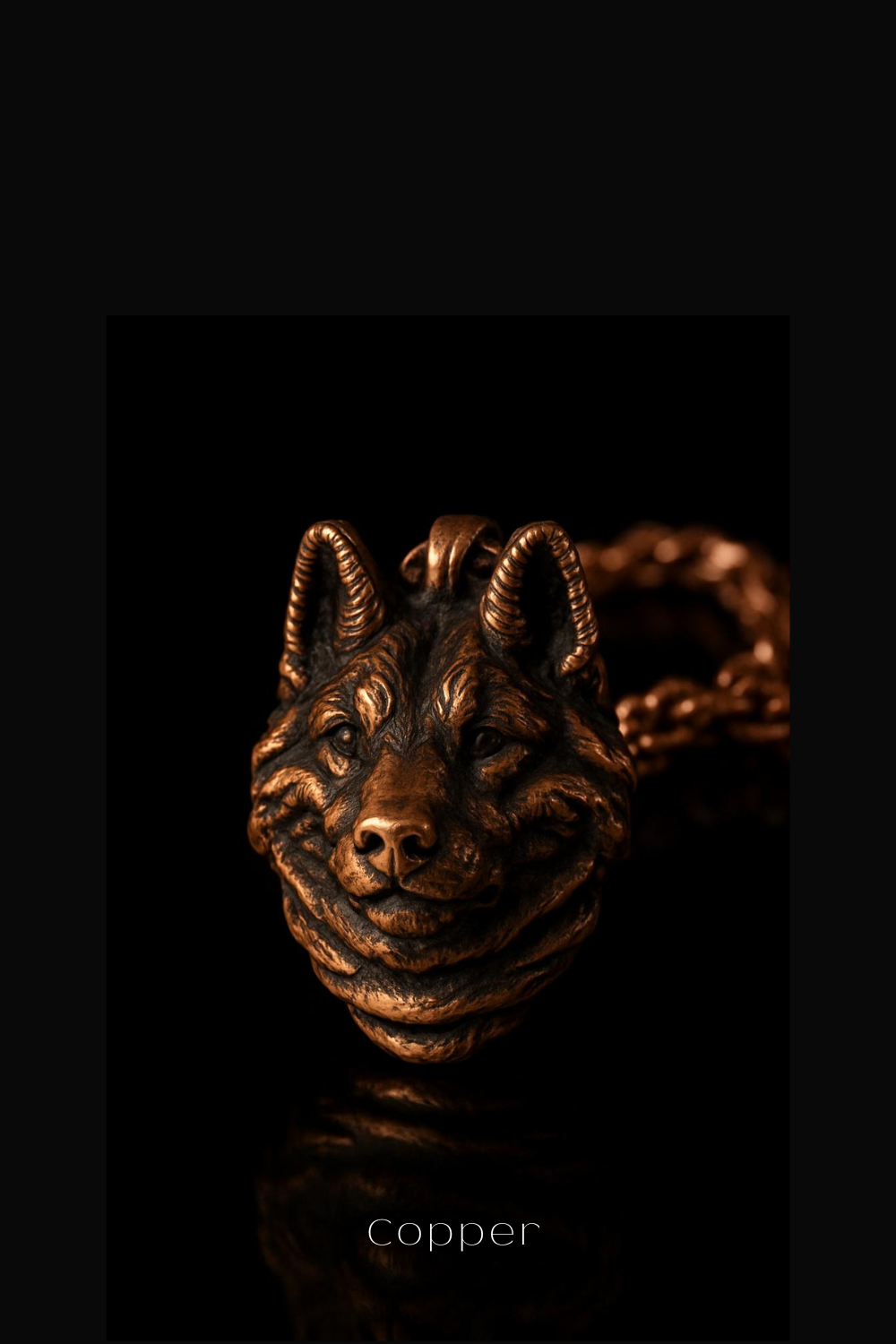 A close-up of a detailed, intricately designed copper pendant in the shape of a wolf's head against a dark background.