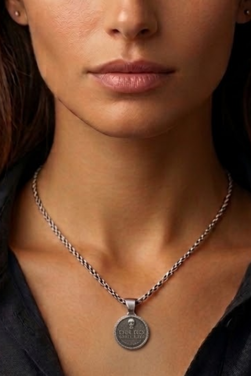 A close-up of a woman's neck and chest area, with a silver necklace and a pendant featuring a small circular design.