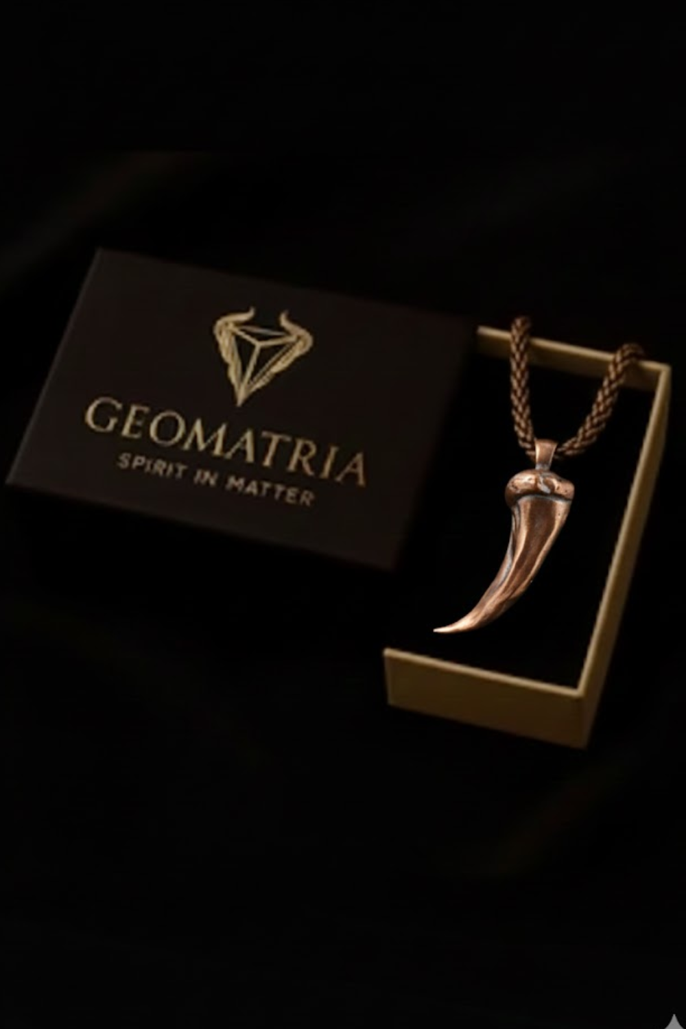 A pendant necklace with a large, ornate pendant is displayed in a black box with the text "Geomatria" and "SPIRIT IN MATER" printed on it.