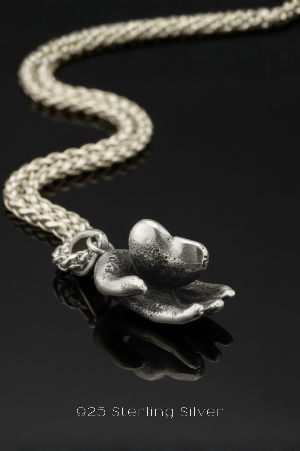 A close-up image of a silver pendant necklace with a heart-shaped charm on a dark background.