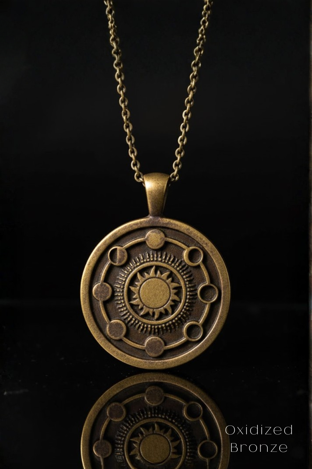A round, ornate pendant with a sun design and celestial elements, suspended from a chain against a black background.
