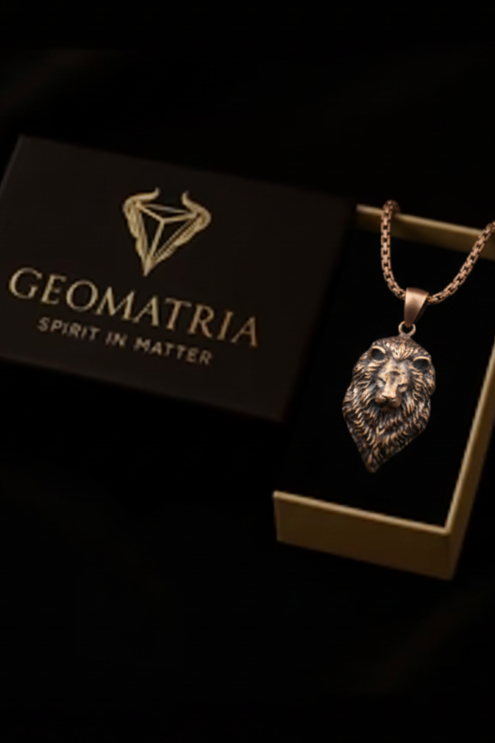 A necklace with a pendant in the shape of a lion's head is displayed in a gold box with the text "Geomatria" and "SPIRIT IN MATTERS" printed on it.