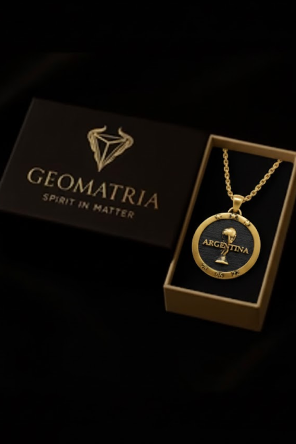 A gold necklace with a pendant featuring the word "ARGENTINA" and a trophy, placed inside a dark box with the word "Geomatria" printed on it.
