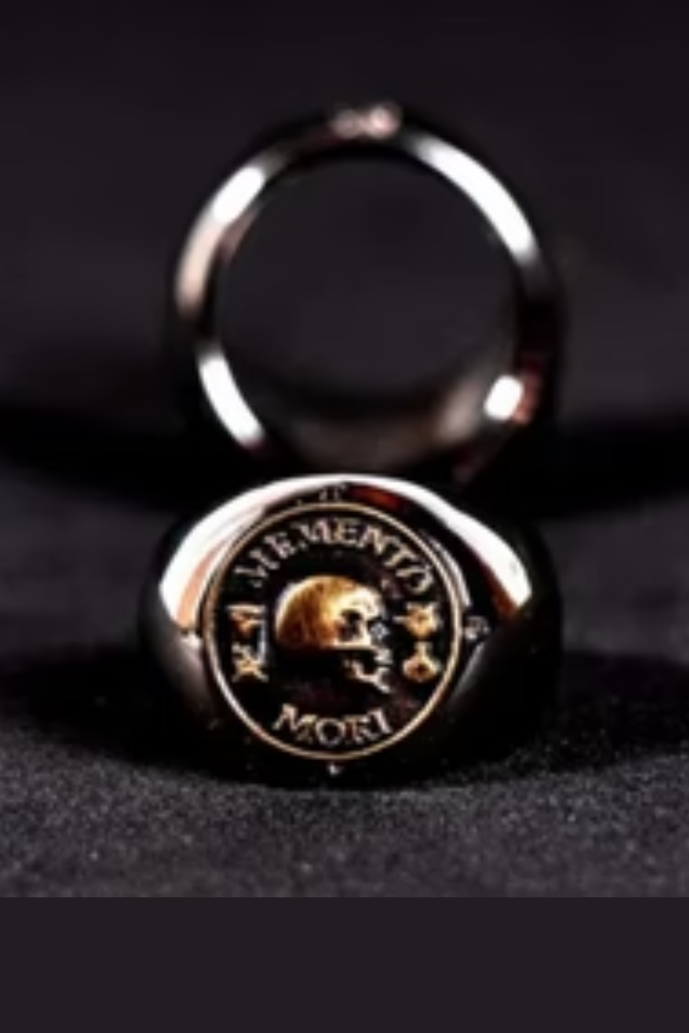 a close-up of a ring with a skull design and the Latin phrase "Memento mori" inscribed on it.