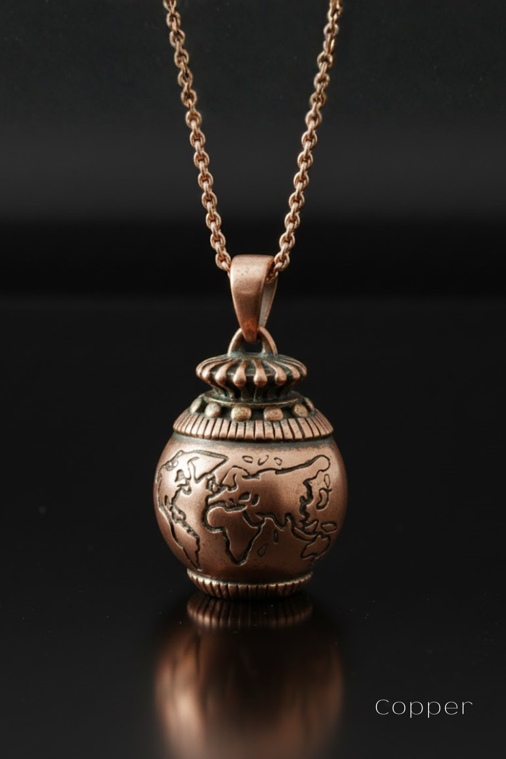 A copper-colored pendant necklace with a globe-shaped design on the front, suspended from a chain against a dark background.