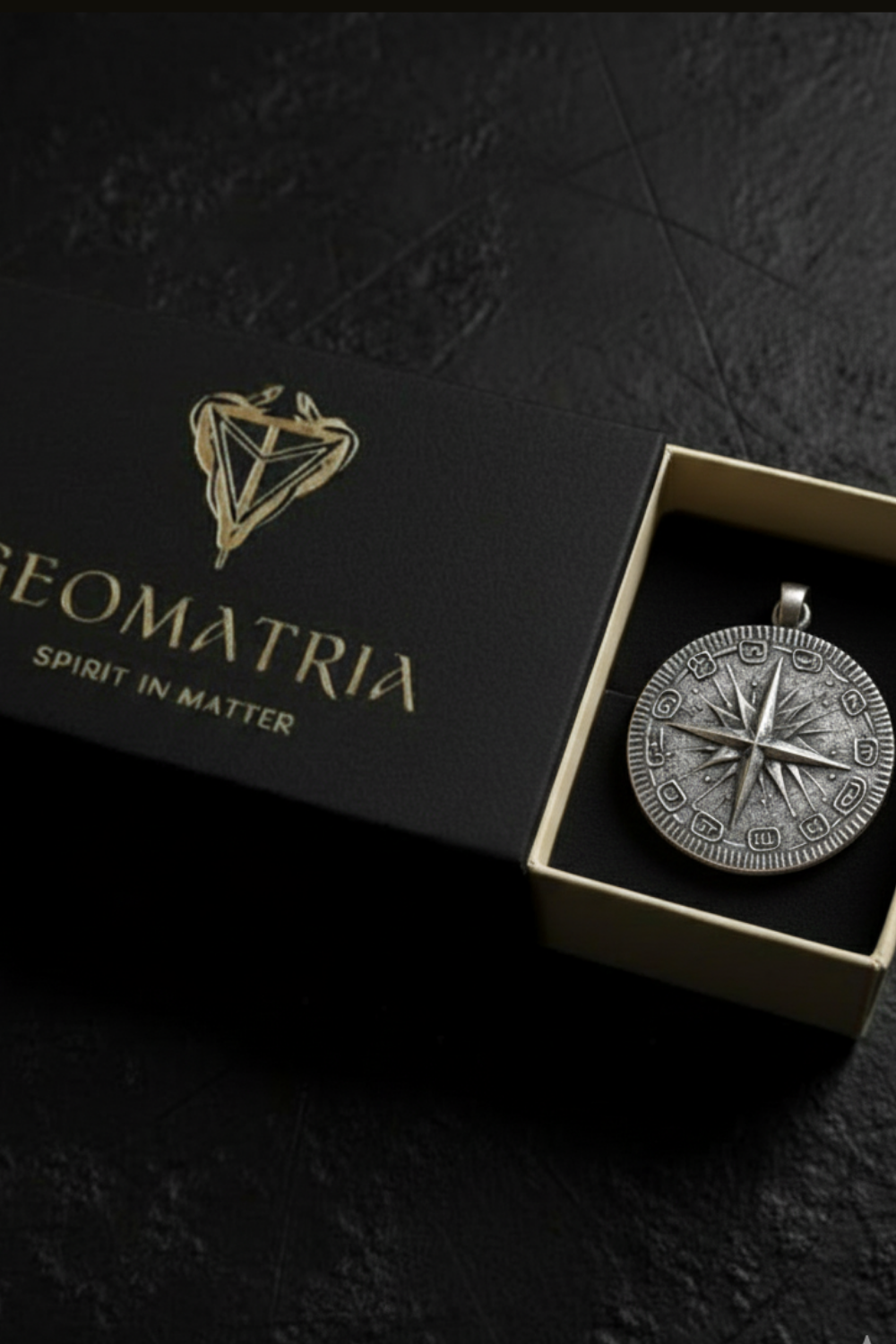 A silver compass pendant is displayed in a black box with the text "Geomatria" and "SPIRIT IN MATTERS" printed on it.