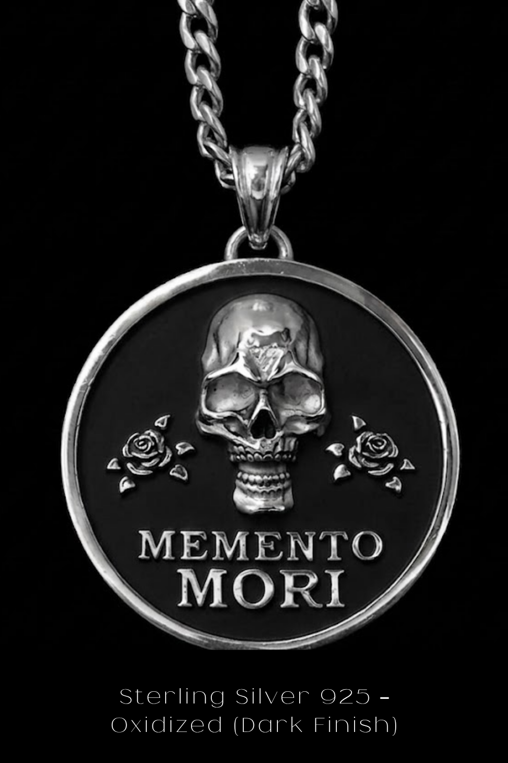 A silver-toned pendant necklace with a circular medallion featuring a skull and two roses, along with the text "MEMENTO MORI" (Memento mori).