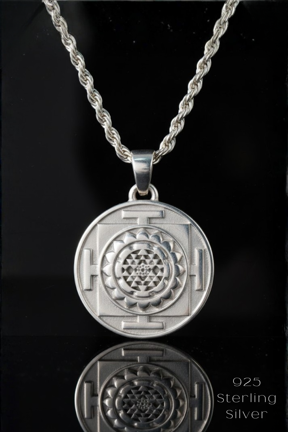 A silver pendant necklace with a circular medallion featuring a symmetrical design, suspended from a chain against a black background.