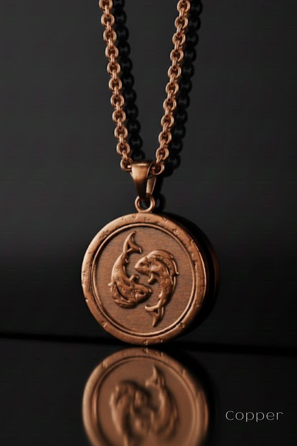 A copper-colored pendant necklace with a circular medallion featuring a fish design, suspended against a dark background.
