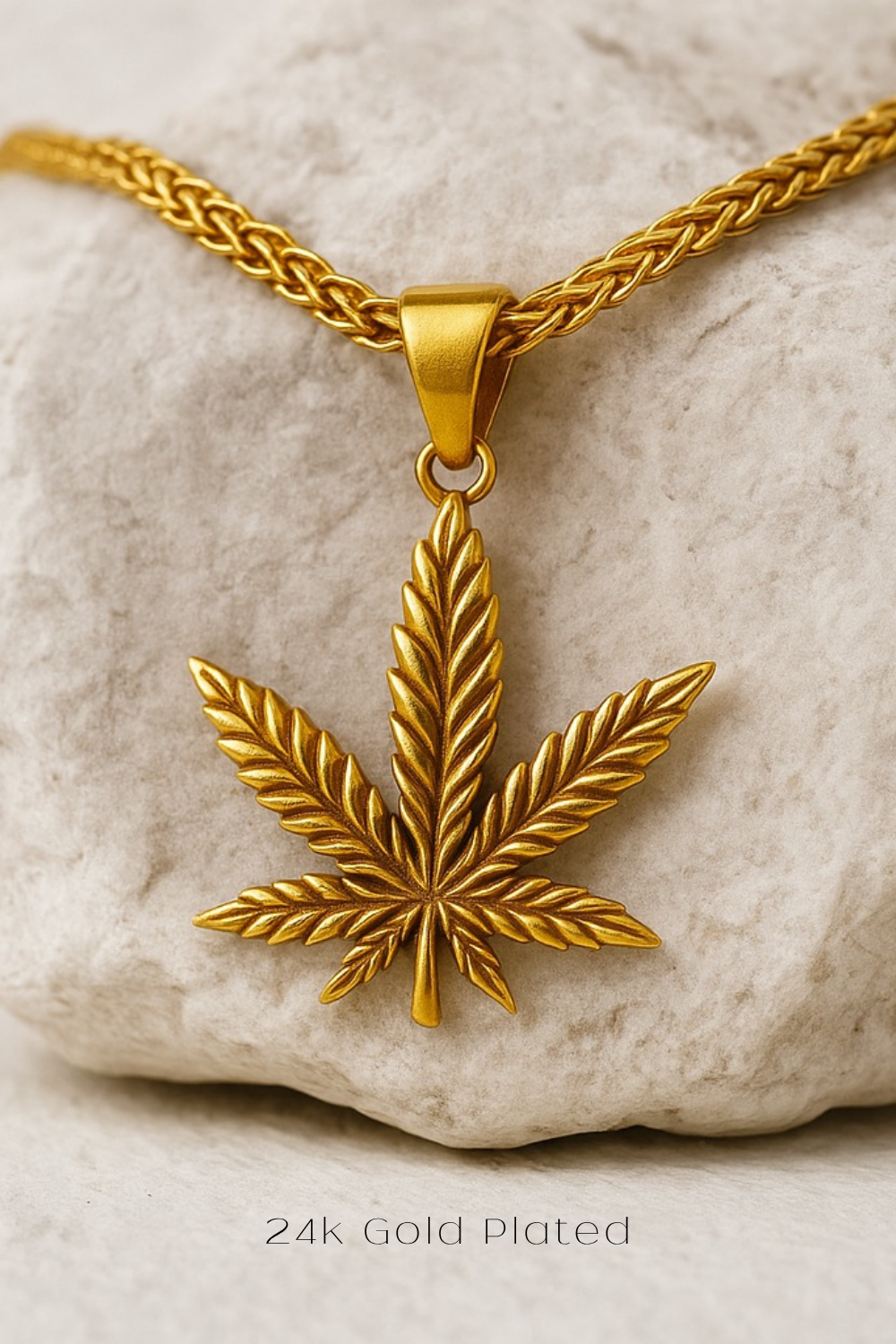 A gold-plated pendant in the shape of a marijuana leaf is displayed against a white background.