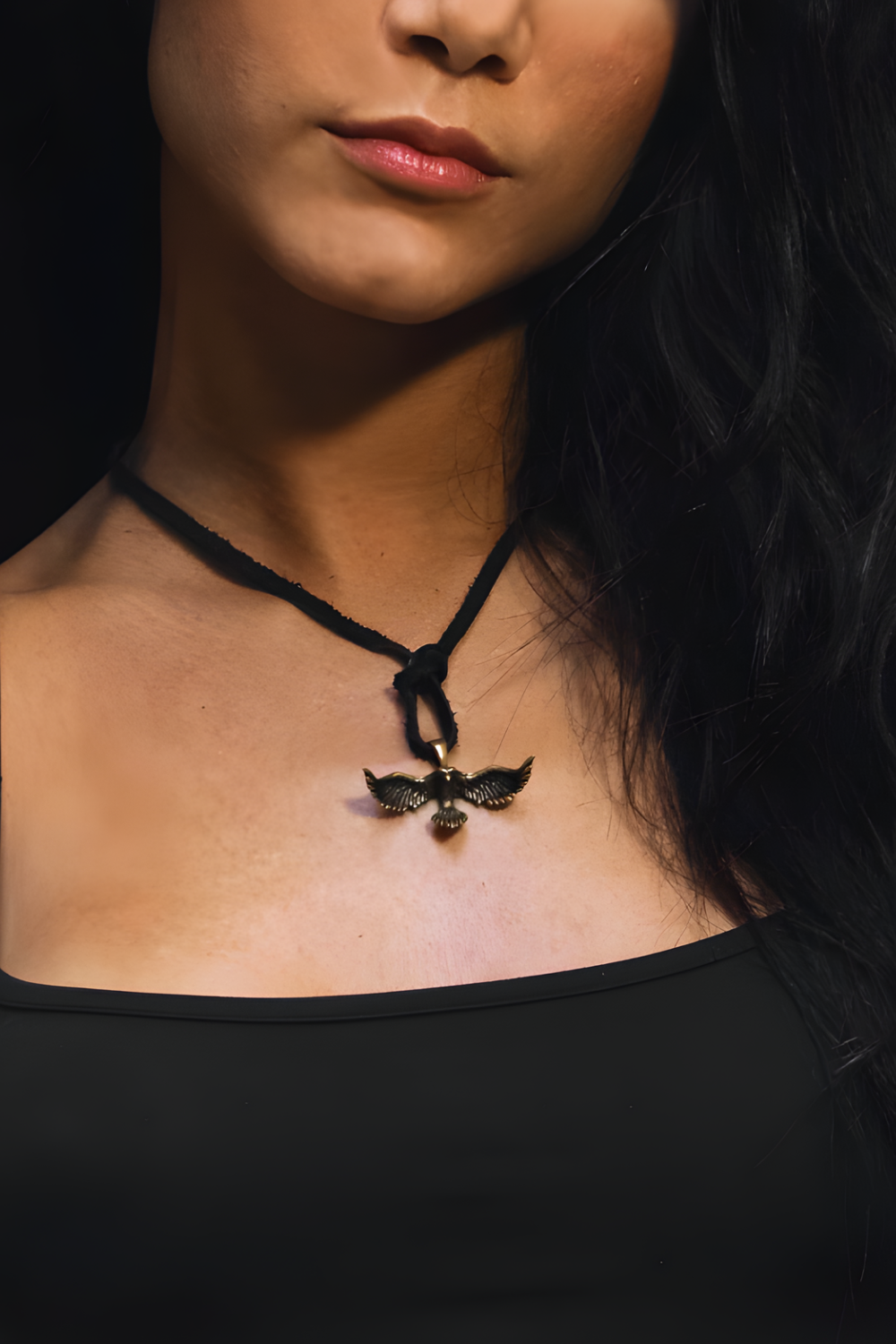 A close-up of a woman's neck and chest area, with a pendant necklace featuring a bird design.