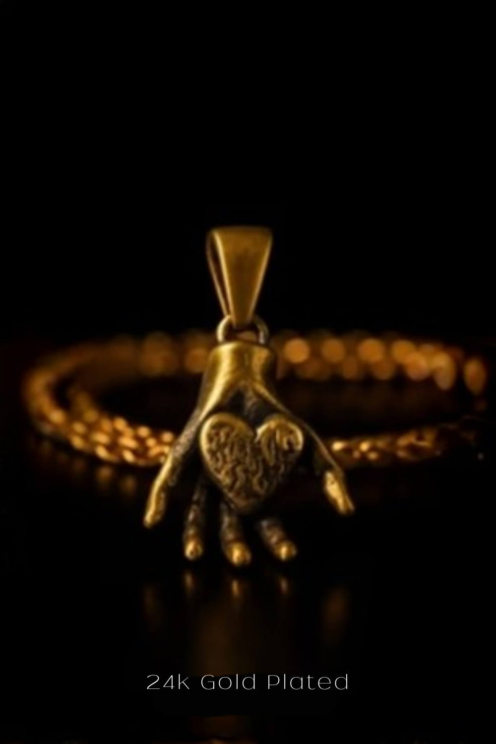 A close-up of a gold-plated pendant in the shape of a hand holding a heart, set against a dark background.