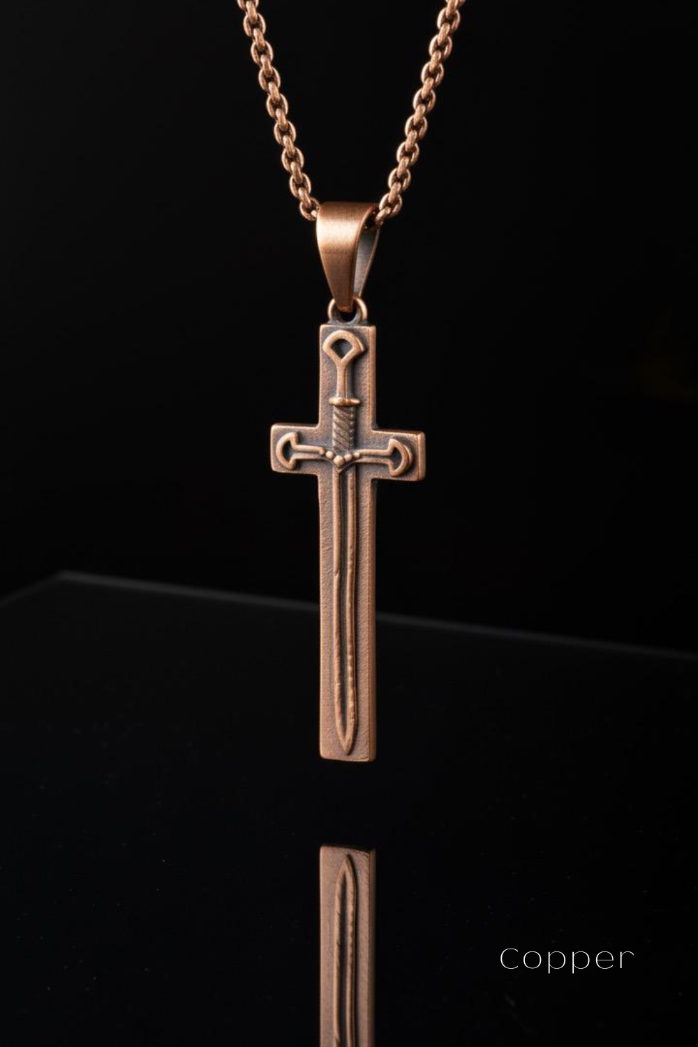 A copper-colored pendant in the shape of a cross, with a sword design, is suspended from a chain against a black background.