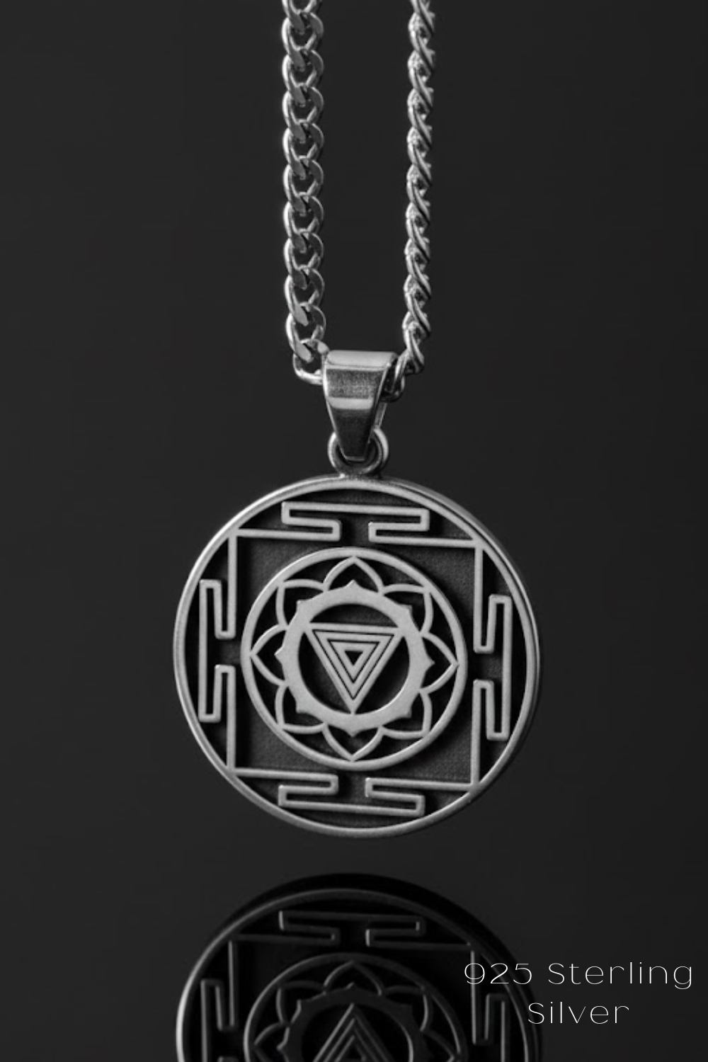 A silver pendant necklace with a circular design featuring a geometric pattern and a central symbol.