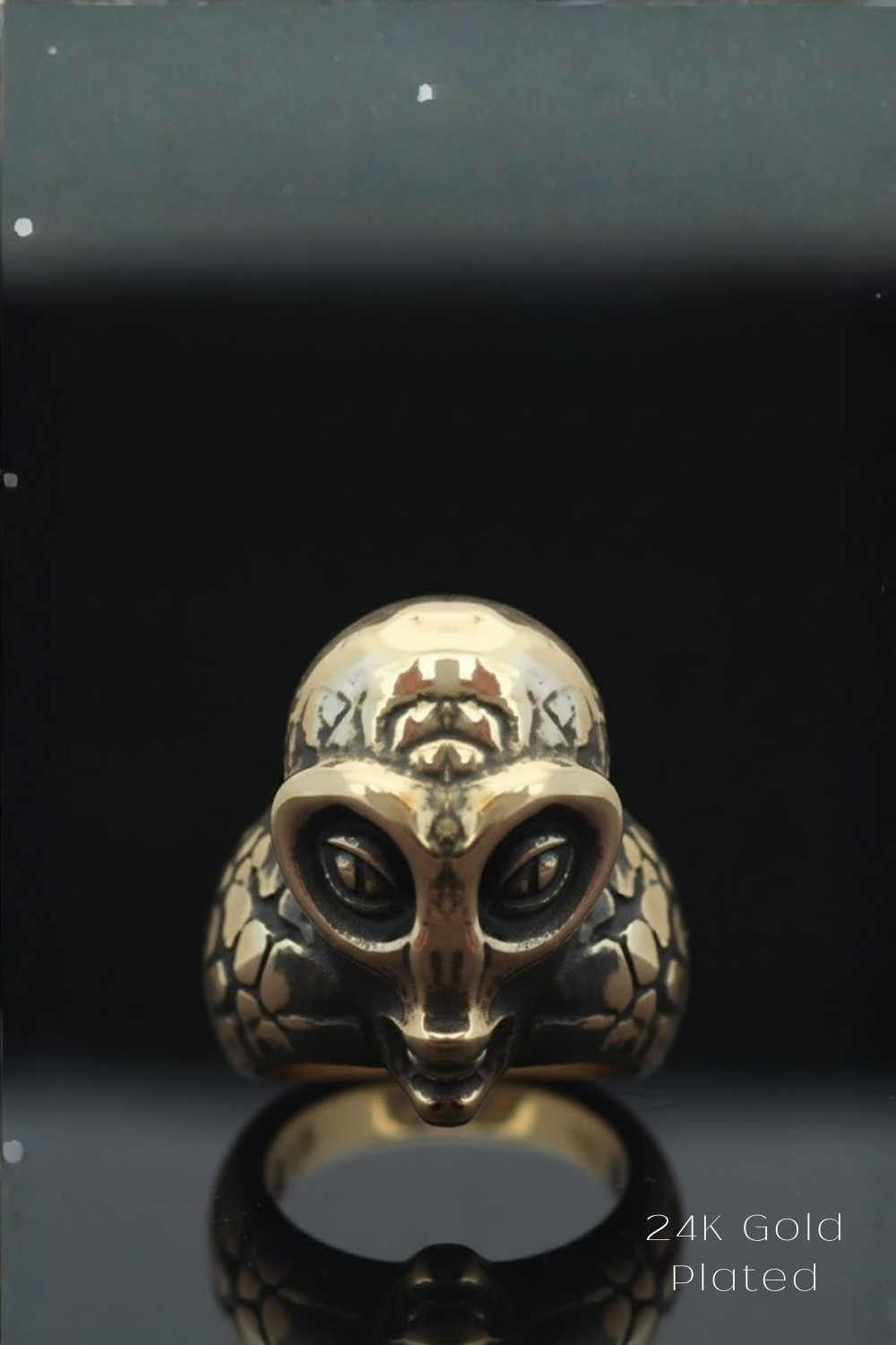 A gold ring with an intricate, alien-like design on the front, set against a black background.