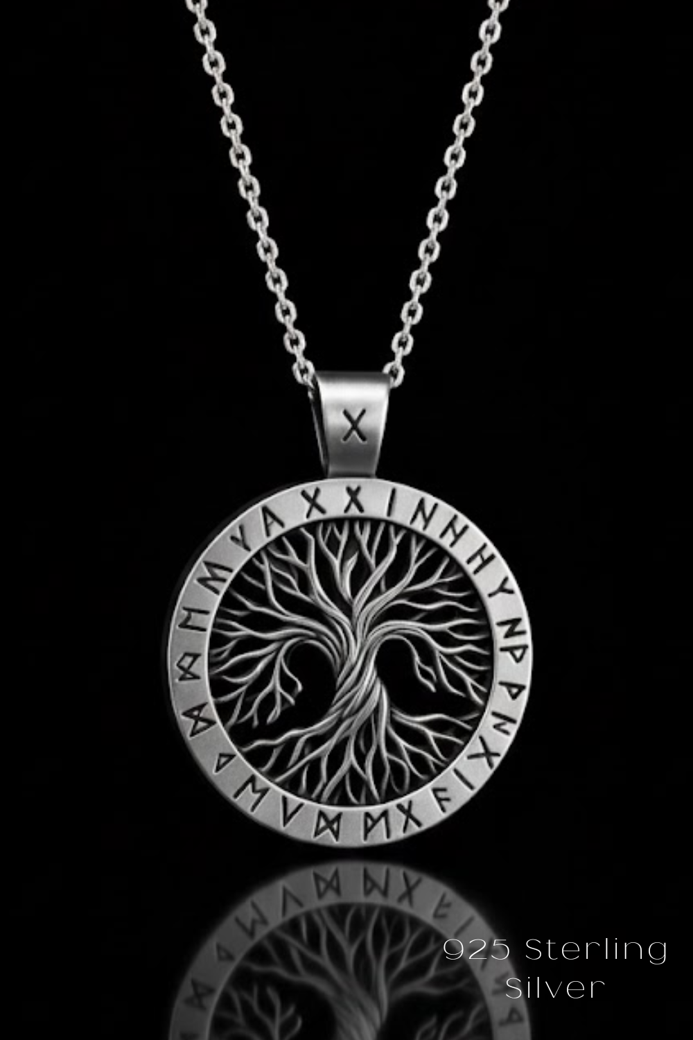 A silver necklace pendant with a circular design featuring a tree-like motif and various symbols, including what appear to be letters and numbers.