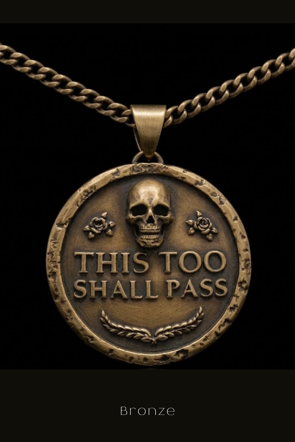 A bronze pendant with a skull design and the text "THIS TOO SHALL PASS" on it.