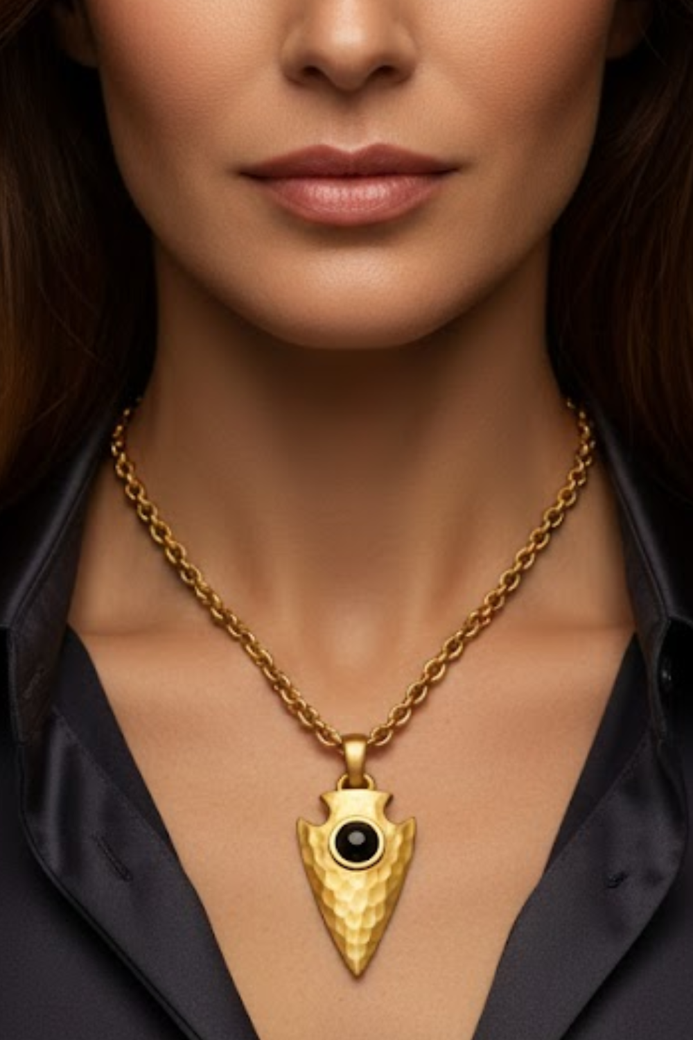 A close-up of a woman's neck and chest area, with a gold necklace featuring a pendant with a black gemstone.