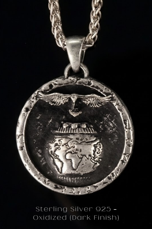A silver pendant with a detailed design, including a bird, a globe, and a chain. The pendant is set against a dark background.