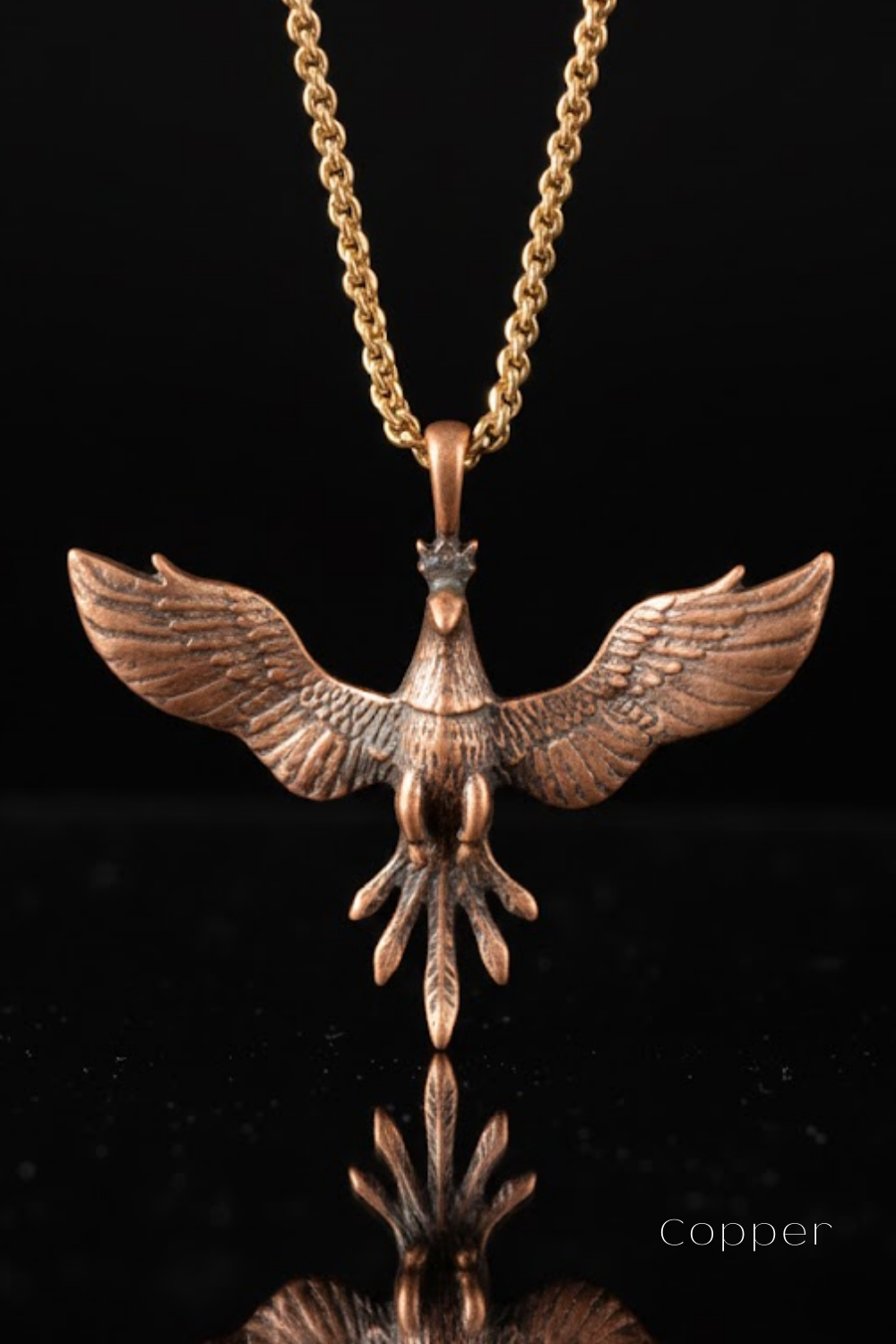 A copper-colored pendant in the shape of a bird, with wings spread wide, is displayed against a black background.
