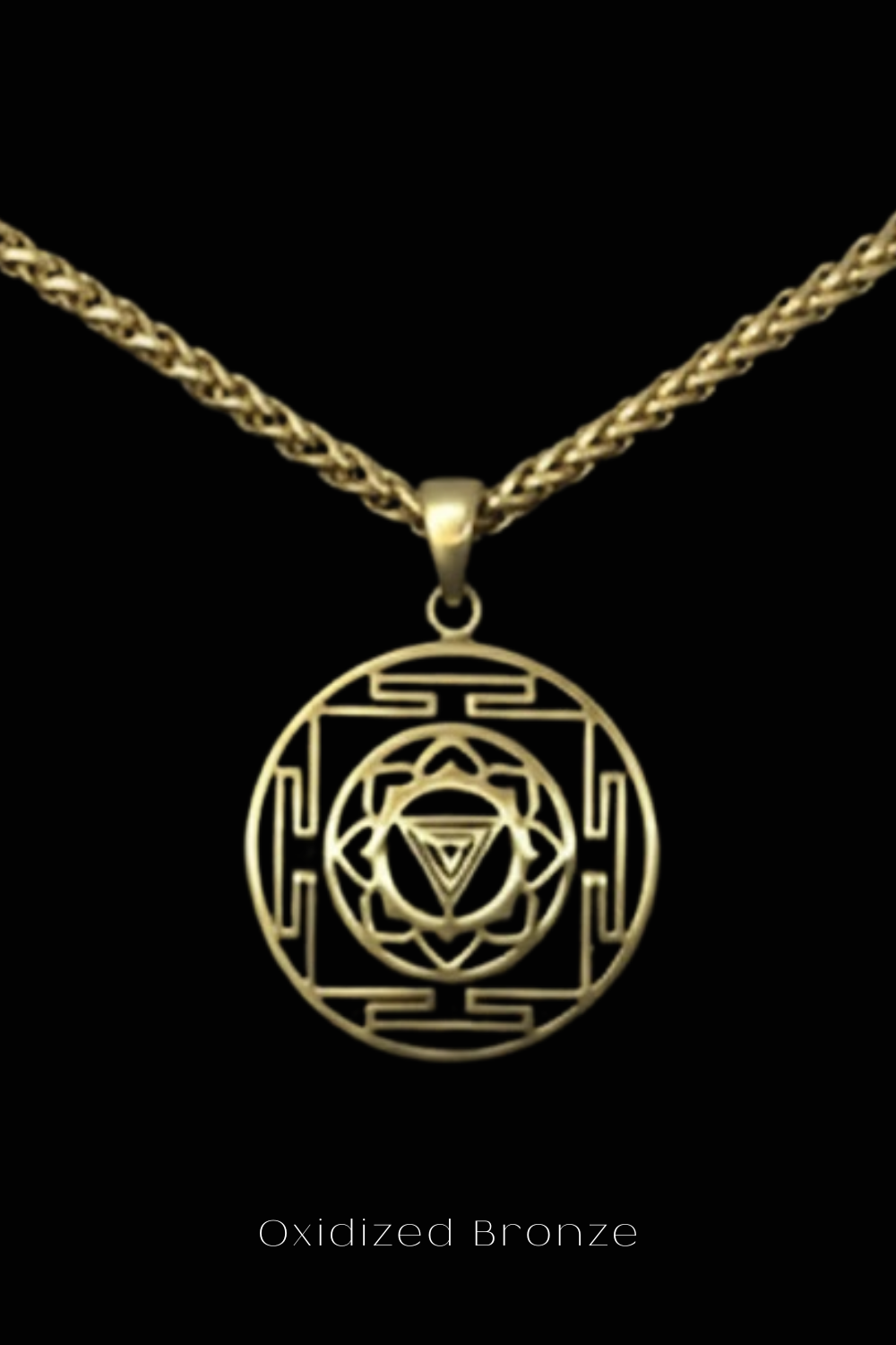 A gold-colored pendant with a circular design featuring a triangle and a floral motif, suspended from a chain against a black background.
