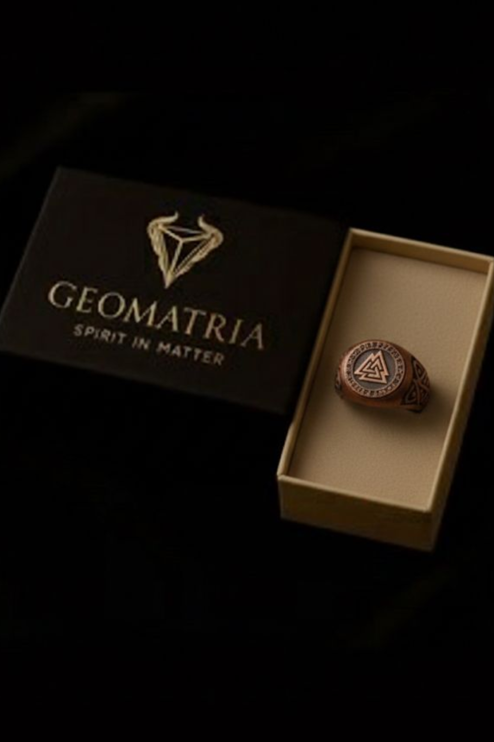 A black box with the word "Geomatria" printed on it, and a gold-colored ring placed inside the box.