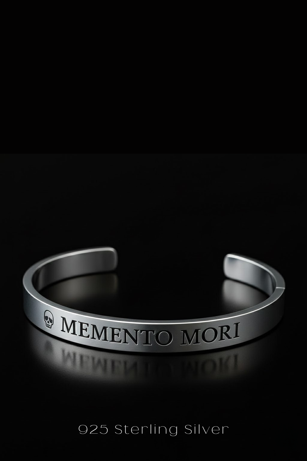 A silver bracelet with the text "MEMENTO MORI" engraved on it, against a black background.